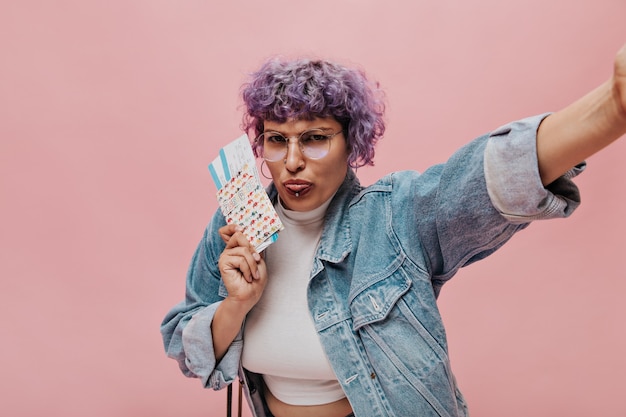 Mujer elegante ofendida en top blanco muestra lengua y tiene entradas. Mujer con gafas toma selfie.