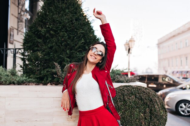 Mujer elegante de pie cerca de árbol verde y expresando felicidad