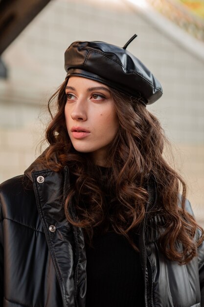 Mujer elegante posando en invierno otoño moda tendencia abrigo negro y sombrero de cuero boina en la vieja calle hermosa con zapatos de tacón alto