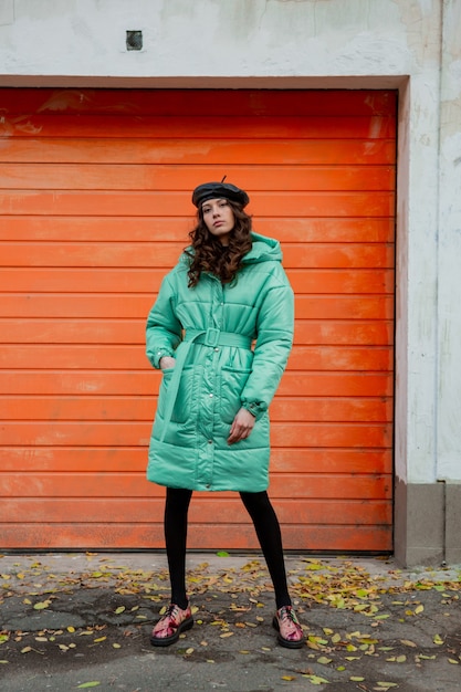 Mujer elegante posando en invierno otoño tendencia de moda abrigo acolchado y sombrero boina contra la pared naranja en la calle vistiendo coloridos zapatos impresos