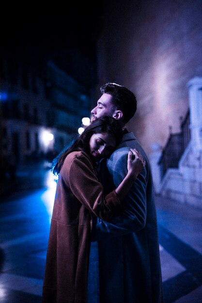 Mujer elegante que abraza con el hombre joven en el paseo en la noche