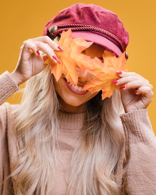 Mujer elegante que cubre sus ojos con hojas de otoño