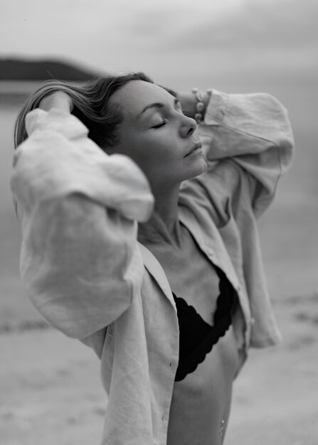 Mujer elegante con ropa informal posando en una playa solitaria en un clima nublado Blanco y negro