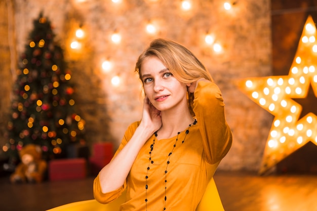 Mujer elegante rubia en habitación con luces de navidad