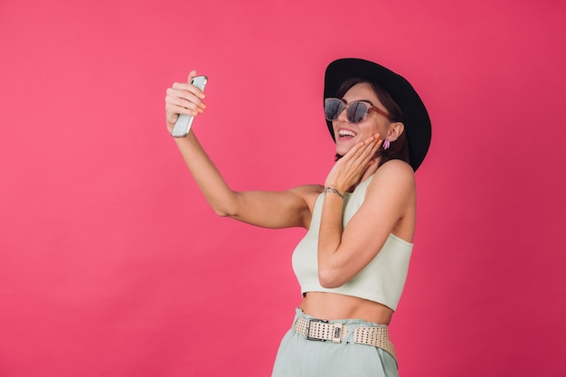 Mujer elegante con sombrero y gafas de sol en la pared roja rosa