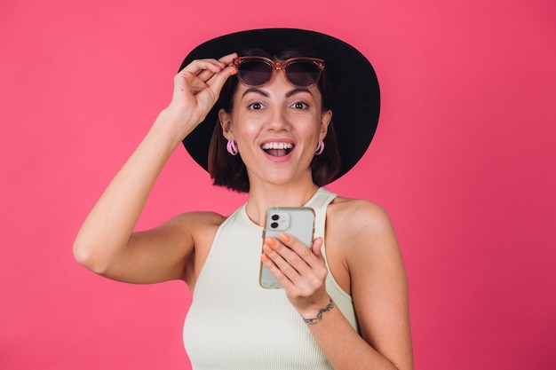 Mujer elegante con sombrero y gafas de sol en la pared roja rosa