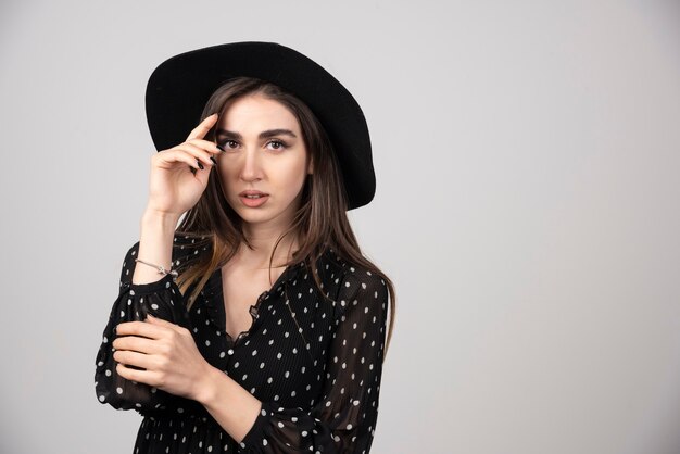 Mujer elegante con sombrero negro mirando a cámara.