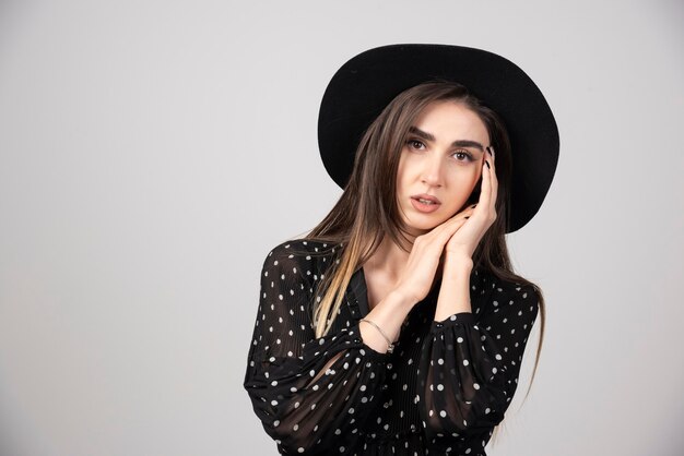 Mujer elegante con sombrero negro sosteniendo su rostro.