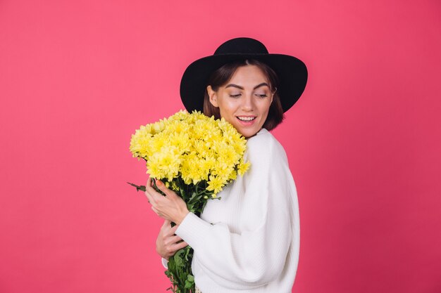 Mujer elegante con sombrero y suéter blanco casual en pared roja