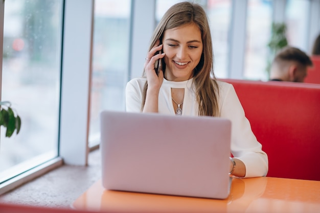 Mujer elegante sonriente hablando por teléfono y mirando su portátil