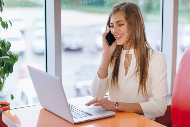 Mujer elegante sonriente hablando por teléfono y la pantalla de su ordenador