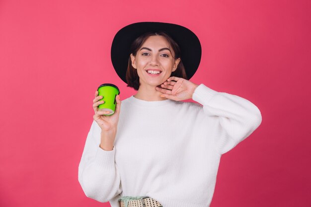 Mujer elegante en suéter blanco casual y sombrero en la pared roja rosa