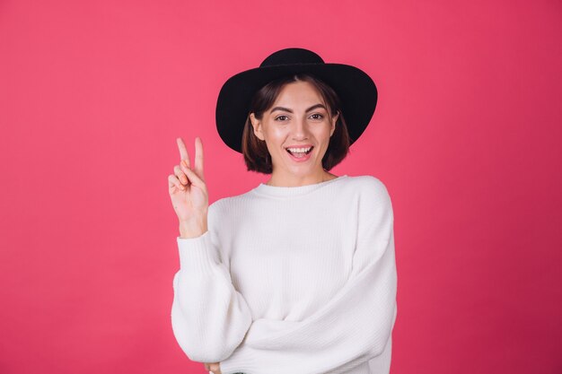 Mujer elegante en suéter blanco casual y sombrero en la pared rosa roja