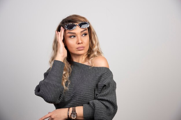 Mujer elegante en suéter gris con anteojos en la cabeza.