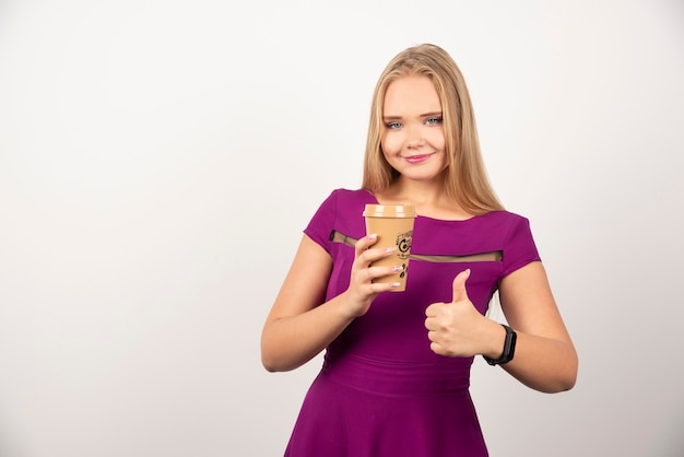 Mujer elegante con taza de café posando y haciendo pulgares.