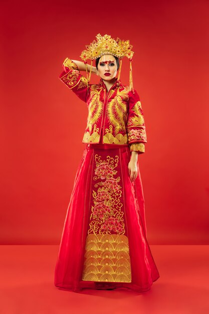 Mujer elegante tradicional china en el estudio sobre fondo rojo. Hermosa chica vestida con traje nacional. Año nuevo chino, elegancia, gracia, ejecutante, actuación, danza, actriz, concepto de emociones