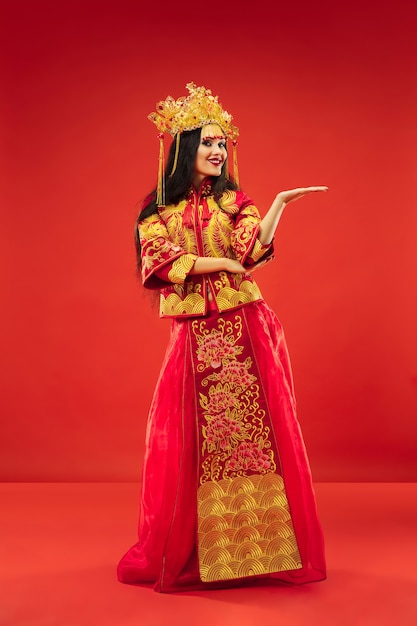 Mujer elegante tradicional china en el estudio sobre fondo rojo. Hermosa chica vestida con traje nacional. Año nuevo chino, elegancia, gracia, ejecutante, actuación, danza, actriz, concepto de vestimenta