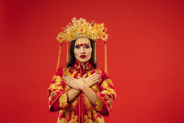 Mujer elegante tradicional china en el estudio sobre fondo rojo. Hermosa chica vestida con traje nacional. Año nuevo chino, elegancia, gracia, ejecutante, actuación, danza, actriz, concepto de vestimenta