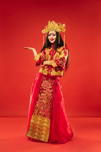 Mujer elegante tradicional china en el estudio sobre la pared roja