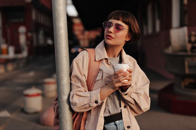 Mujer elegante en traje ajustado sosteniendo una taza de té en la ciudad