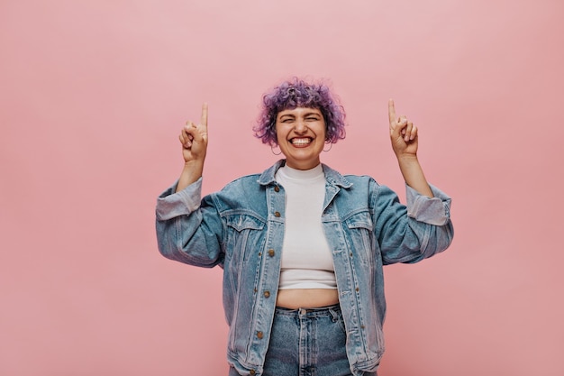 Foto gratuita mujer elegante en traje de mezclilla y con aretes redondos levanta los dedos y se ríe. mujer sonriente en chaqueta de gran tamaño posando en rosa.