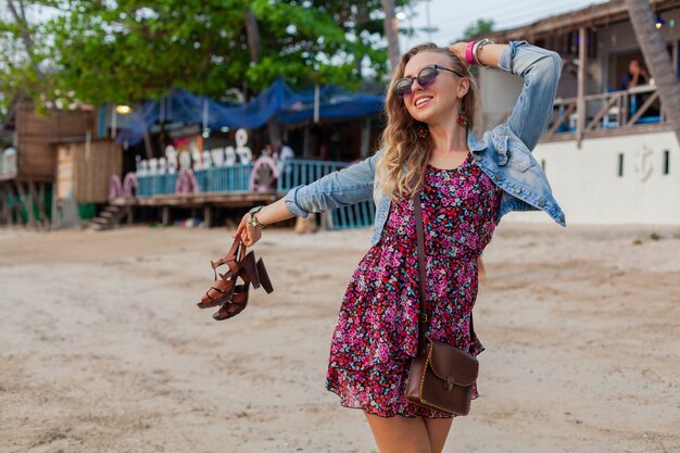 Mujer elegante en vacaciones de vestido de verano caminando en la playa con zapatos en mano