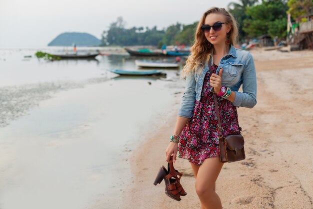 Mujer elegante en vacaciones de vestido de verano caminando en la playa con zapatos en mano