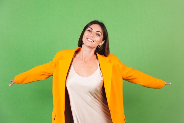 Mujer elegante en vestido beige de seda y blazer naranja de gran tamaño en verde, sonrisa de emociones positivas