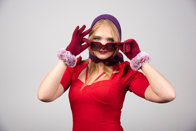 Mujer elegante en vestido rojo sosteniendo sus gafas.