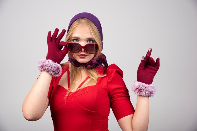 Mujer elegante en vestido rojo sosteniendo sus gafas.