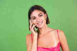 Foto gratuita mujer elegante en vestido de seda rosa aislado en verde feliz con teléfono móvil con gran sonrisa, tener conversación de llamada