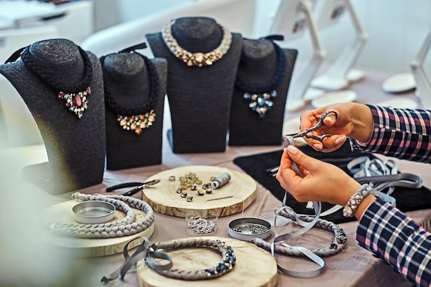 Mujer elegantemente vestida hace collares hechos a mano, trabajando con agujas e hilo en taller de joyería.