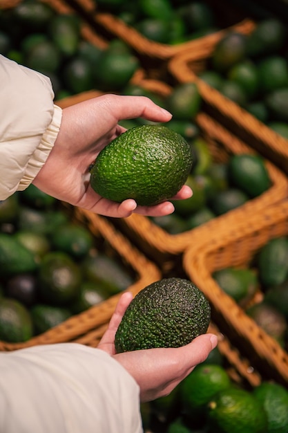 Una mujer elige un aguacate en una tienda de comestibles