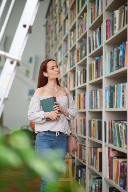 Mujer eligiendo libros cerca de estanterías en la biblioteca