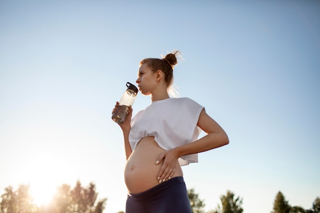 Mujer embarazada bebiendo agua después de hacer ejercicio al aire libre