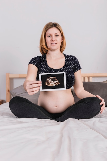 Foto gratuita mujer embarazada en cama enseñando ultrasonido