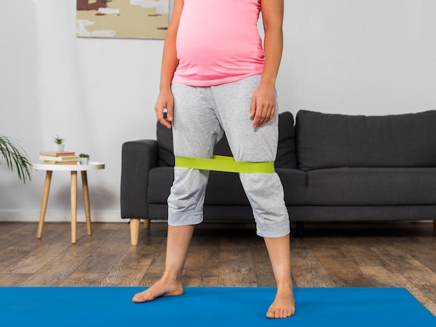Foto gratuita mujer embarazada en casa haciendo ejercicio con banda elástica