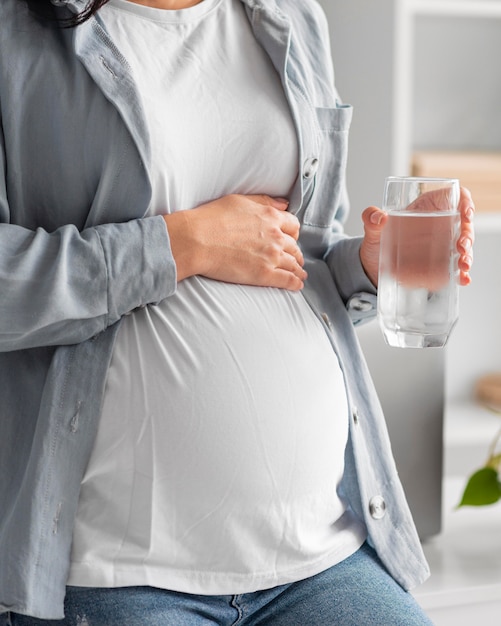 Mujer embarazada en casa sosteniendo un vaso de agua