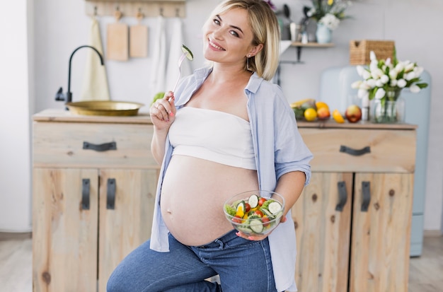 Mujer embarazada comiendo ensalada mientras mira a la cámara