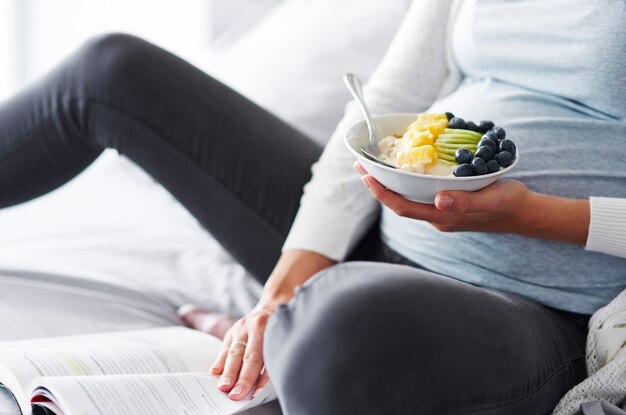 Mujer embarazada comiendo y leyendo un libro en el dormitorio