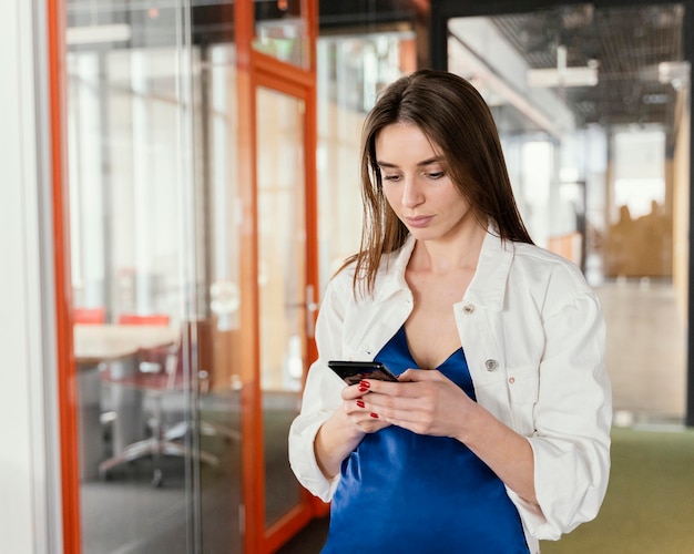 Mujer embarazada comprobando su teléfono en el trabajo