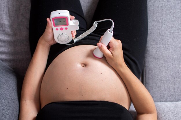 Mujer embarazada con doppler fetal escuchando el corazón del bebé sentado