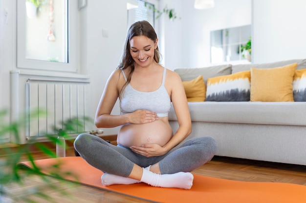 Mujer embarazada entrenando yoga acariciando su vientre Joven expectante feliz relajándose pensando en su bebé y disfrutando de su vida futura Concepto de yoga de embarazo de maternidad