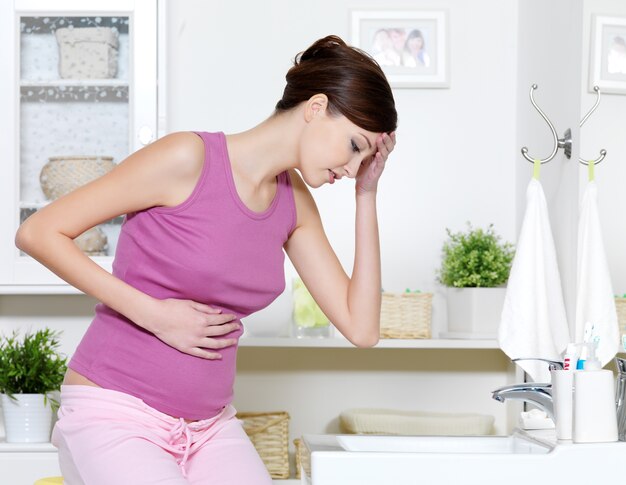 Mujer embarazada con fuerte dolor de estómago y náuseas sentada en el baño.