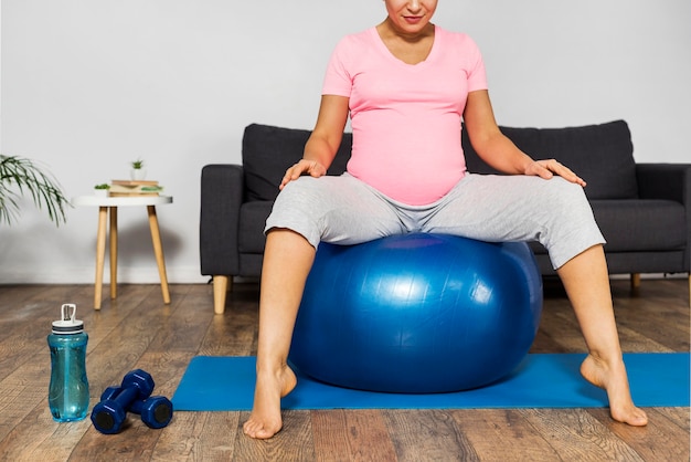 Foto gratuita mujer embarazada haciendo ejercicio en casa en el suelo con pelota y botella de agua