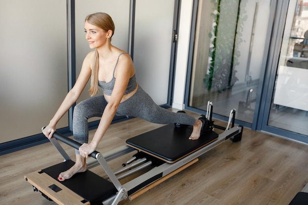 Mujer embarazada haciendo ejercicios con un equipo especial Mujer rubia en forma haciendo ejercicio en un gimnasio Mujer con top y leggins deportivos grises