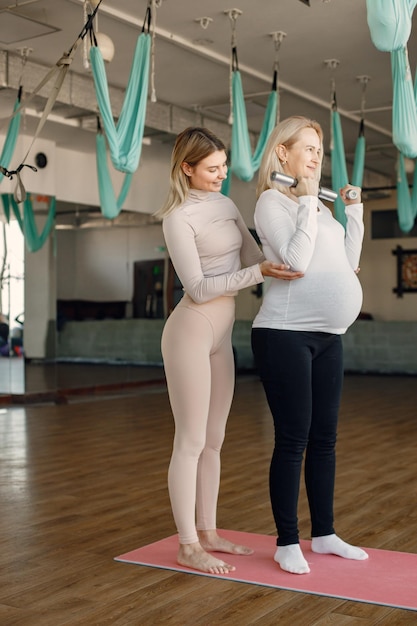 Foto gratuita mujer embarazada haciendo yoga con entrenador personal entrenador de yoga ayudando a la mujer embarazada mientras hace ejercicios con fitball y pesas mujer embarazada rubia con camisa blanca