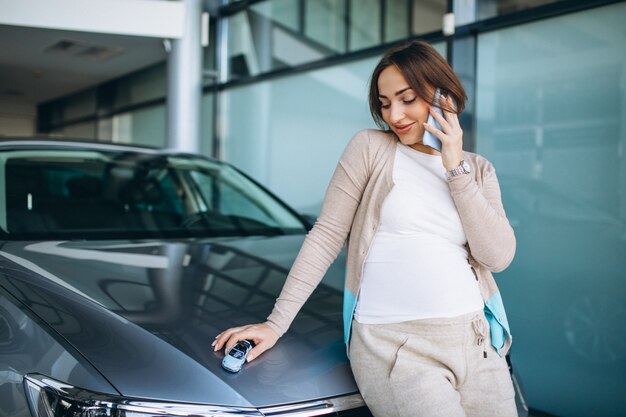 Mujer embarazada joven que elige un coche en una sala de exposición de automóviles