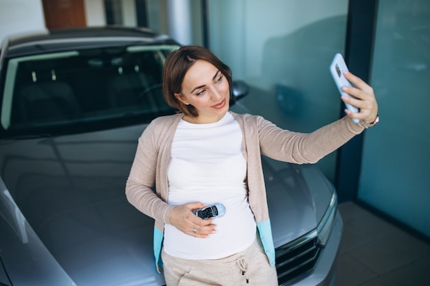 Mujer embarazada joven que elige un coche en una sala de exposición de automóviles