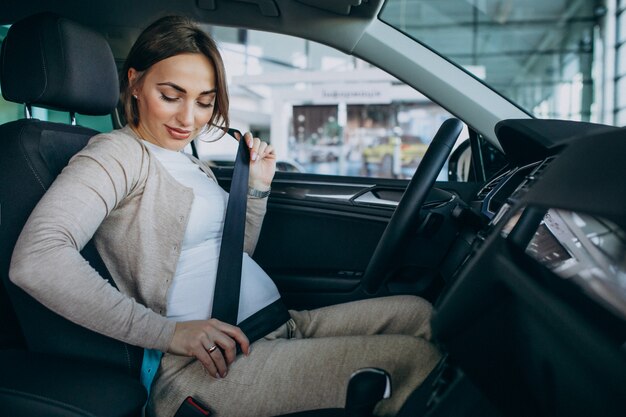 Mujer embarazada joven que prueba un coche en la sala de exposición de automóviles